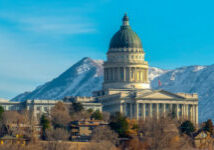 Utah State Capital Building viewed on a sunny day. The grand Utah State Capital Building towering over Salt Lake City. A scenic view of snowy mountain and blue sky can be seen in the background.